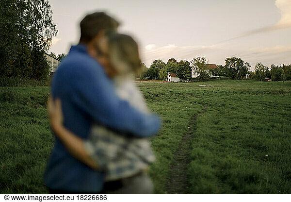 Couple hugging each other with agricultural field in background during sunset