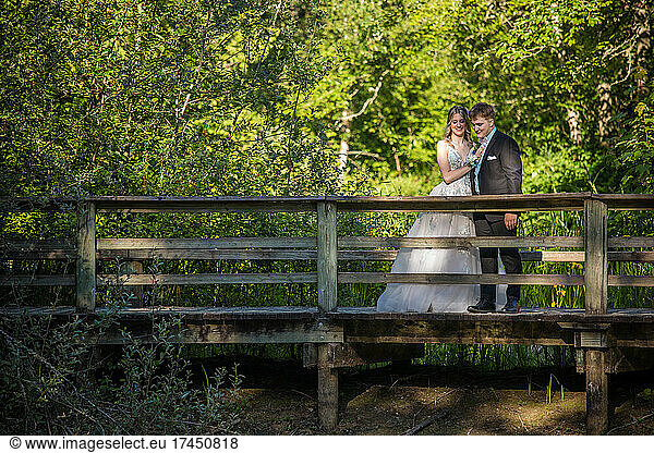 Couple in formal clothes standing on wooden bridge in nature.