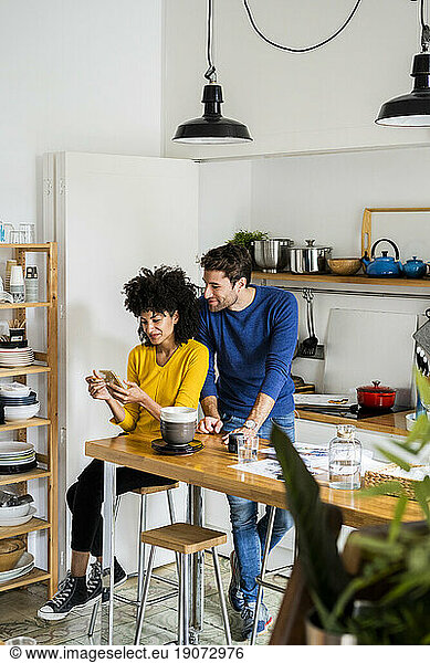 Couple in kitchen at home sharing cell phone