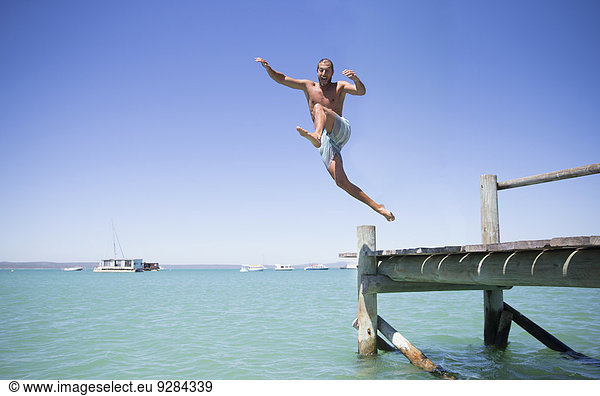Couple jumping off wooden dock into water