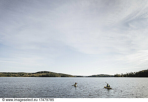 Couple kayaking on lake against sky during weekend