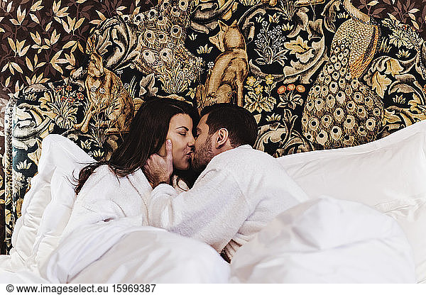 Couple kissing while lying on bed in hotel room