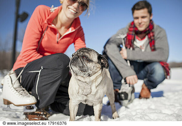 Couple kneeling in the snow with pet pug dog.