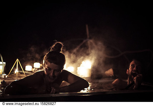 couple laugh in outdoor bath at night with candles