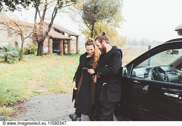 Couple leaning against car looking at smartphone