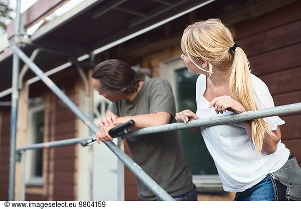 Couple leaning on scaffolding outside house during home improvement