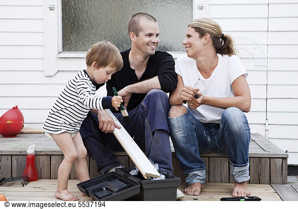 Couple looking at each other while boy painting plank
