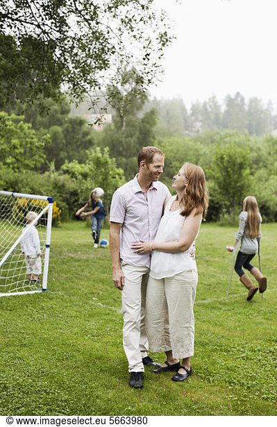 Couple looking at each other with children playing in background