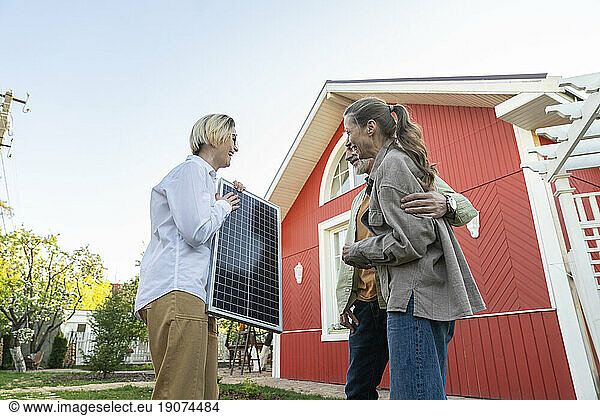 Couple looking at solar panel held by agent in front of house