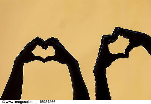 Couple mankink heart shape finger frames against yellow background