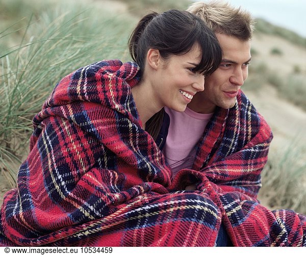 Couple on beach wearing blanket