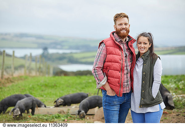 Couple on pig farm looking at camera smiling