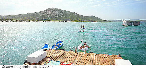 Couple paddleboarding and floating on inflatable raft on sunny lake