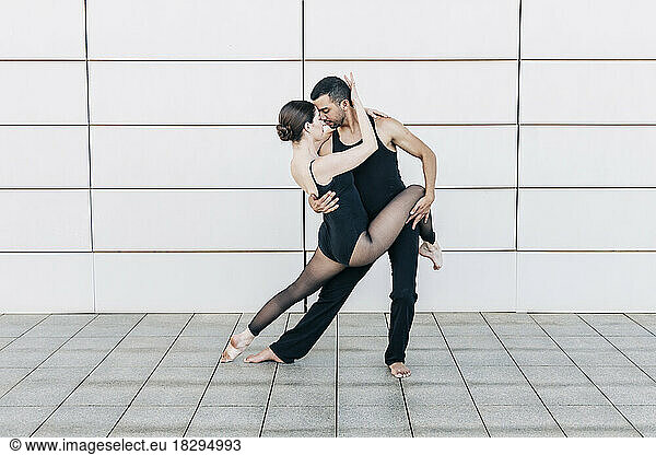 Couple performing ballet dance in front of wall