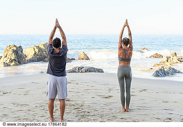 couple practicing yoga at the beach