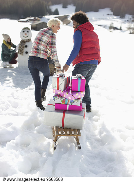 Couple pulling sled with Christmas gifts in snow