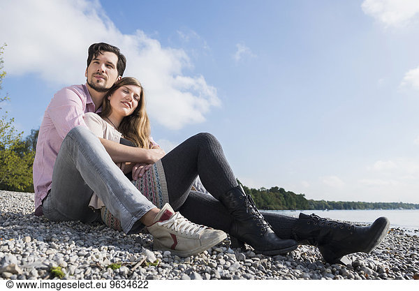 Couple sitting hugging lake shore happy