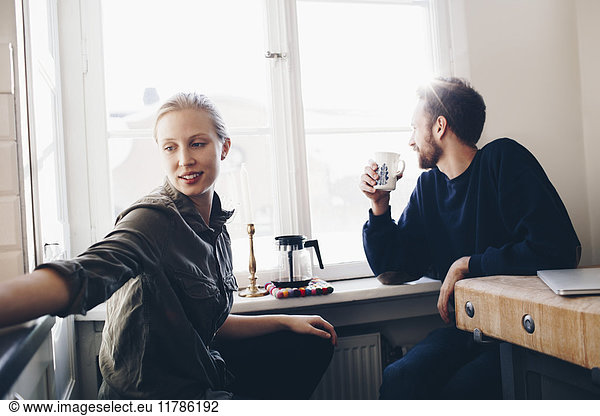 Couple sitting in kitchen drinking coffee by window at home
