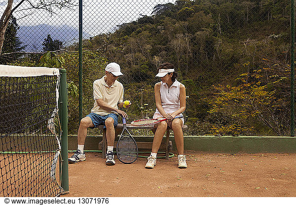 Couple sitting on bench at tennis court
