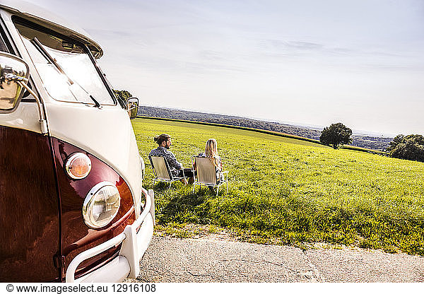 Couple sitting on camping chairs next to van in rural landscape