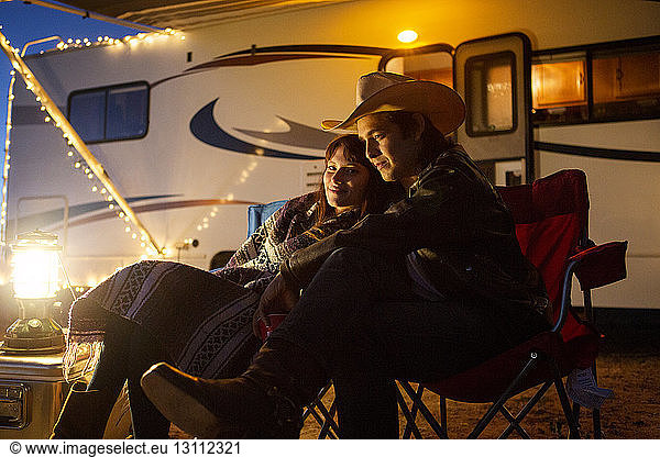 Couple sitting on chairs against camper van during night