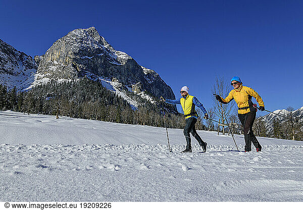 Couple skiing on snowcapped landscape by rocky mountain