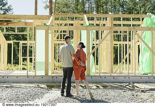 Couple standing and talking near construction frame on sunny day