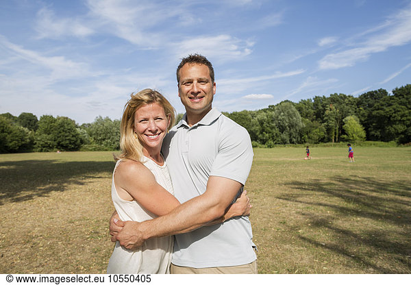 Couple standing in a park  smiling and embracing.