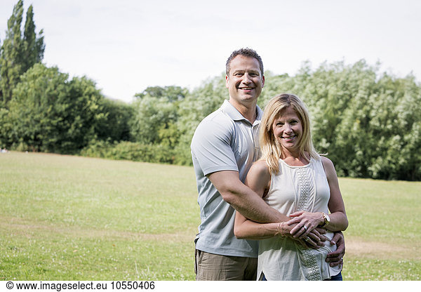 Couple standing in a park  smiling and embracing.