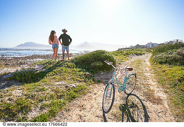 Couple standing on sunny sandy summer ocean beach with bicycle