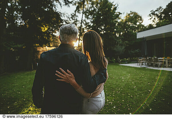 Couple standing with arms around in garden at sunset