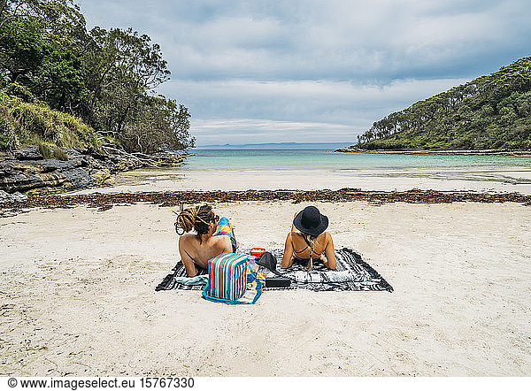 Couple sunbathing on remote tropical ocean beach Jervis Bay Australia