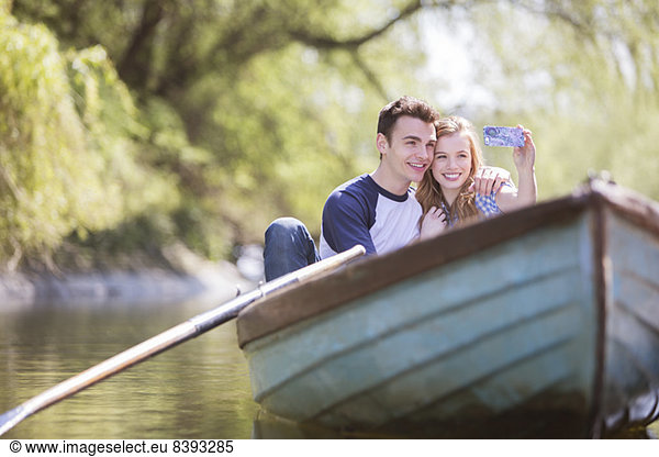 Couple taking self-portraits in rowboat