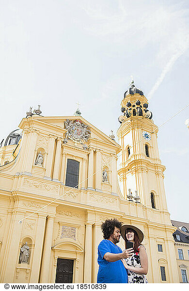 Couple taking selfie using mobile camera in front of Theatiner Church  Munich  Germany