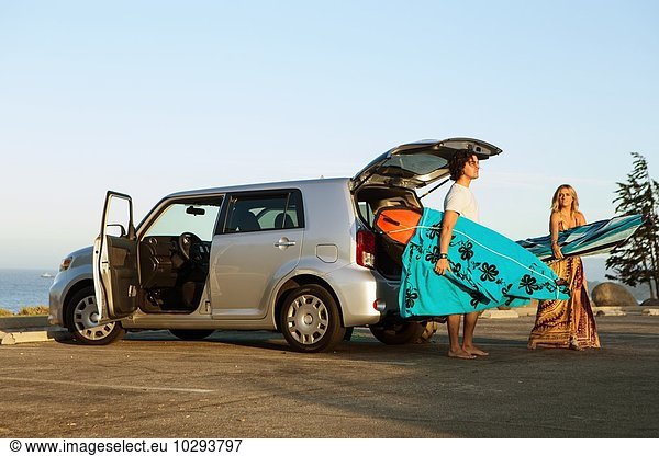 Couple taking surfboards from boot of car