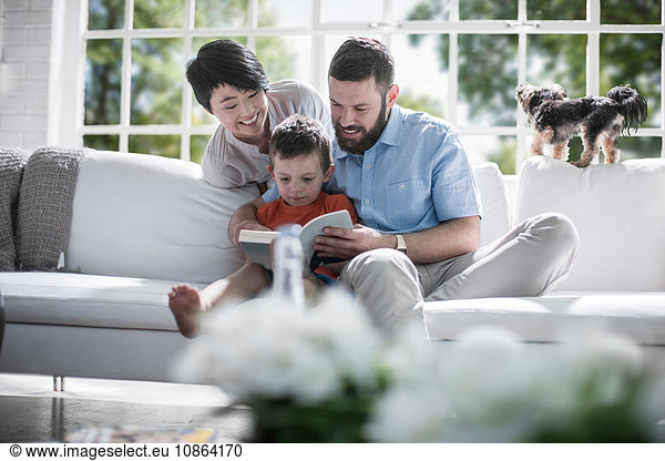 Couple teaching son to read book on sofa