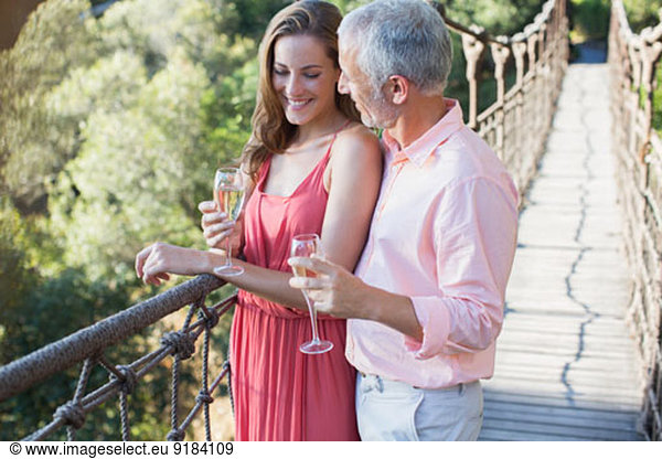 Couple toasting each other on wooden rope bridge