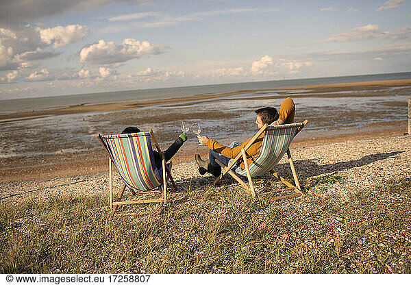 Couple toasting wine glasses from chairs on sunny winter beach