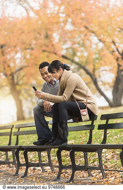 Couple using cell phone on park bench