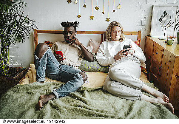 Couple using smart phones resting on bed at home