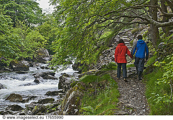 Couple walking hand in hand along a stream at Snowdonia National Park