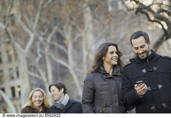 Couple walking in urban park with smartphone