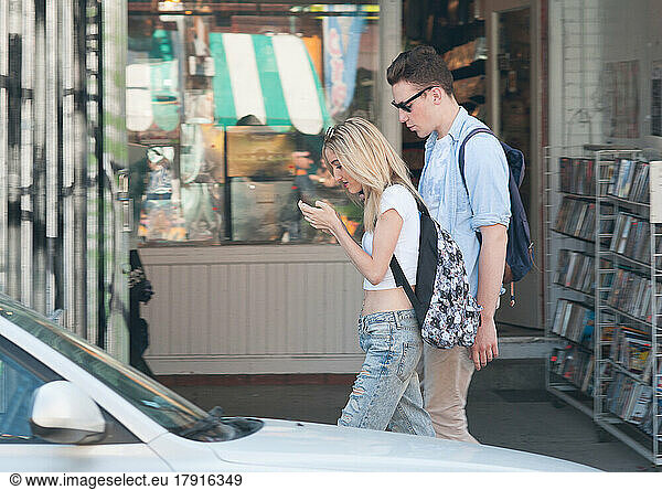 Couple walking on sidewalk  woman looking down at her phone  texting while walking.