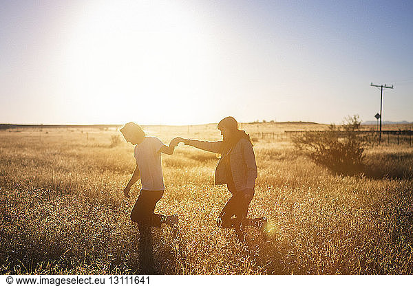 Couple walking while holding hands on field against clear sky