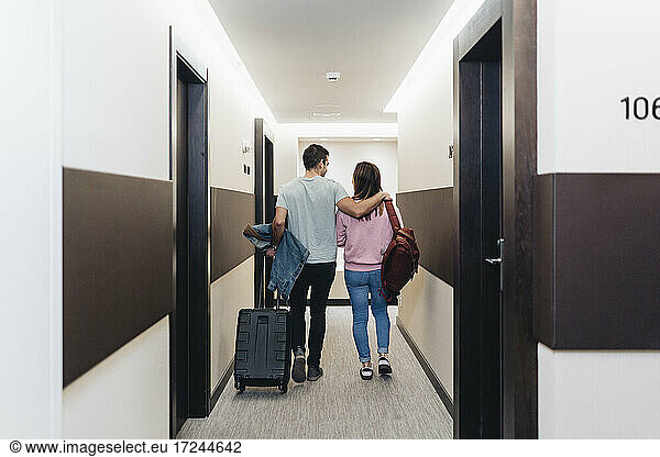 Couple walking with luggage at hotel corridor