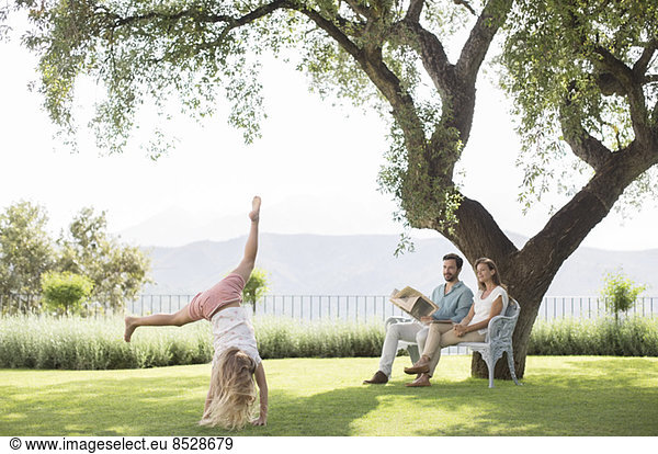 Couple watching daughter do cartwheel outdoors