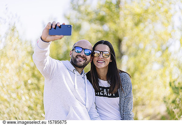 Couple wearing sunglasses and taking a selfie in a park