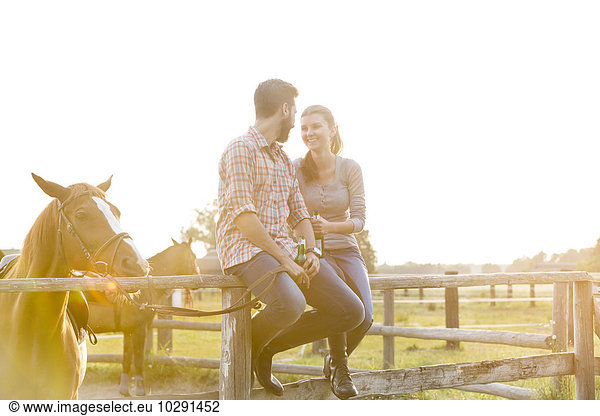 Couple with horse talking on sunny rural pasture fence