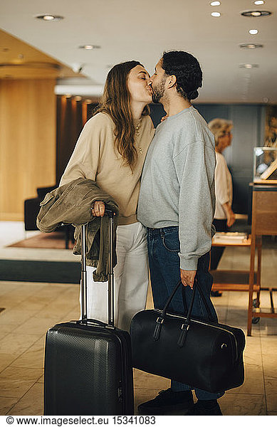 Couple with luggage kissing while standing in hotel lobby