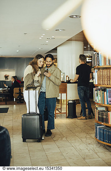 Couple with luggage using smart phone while standing in restaurant